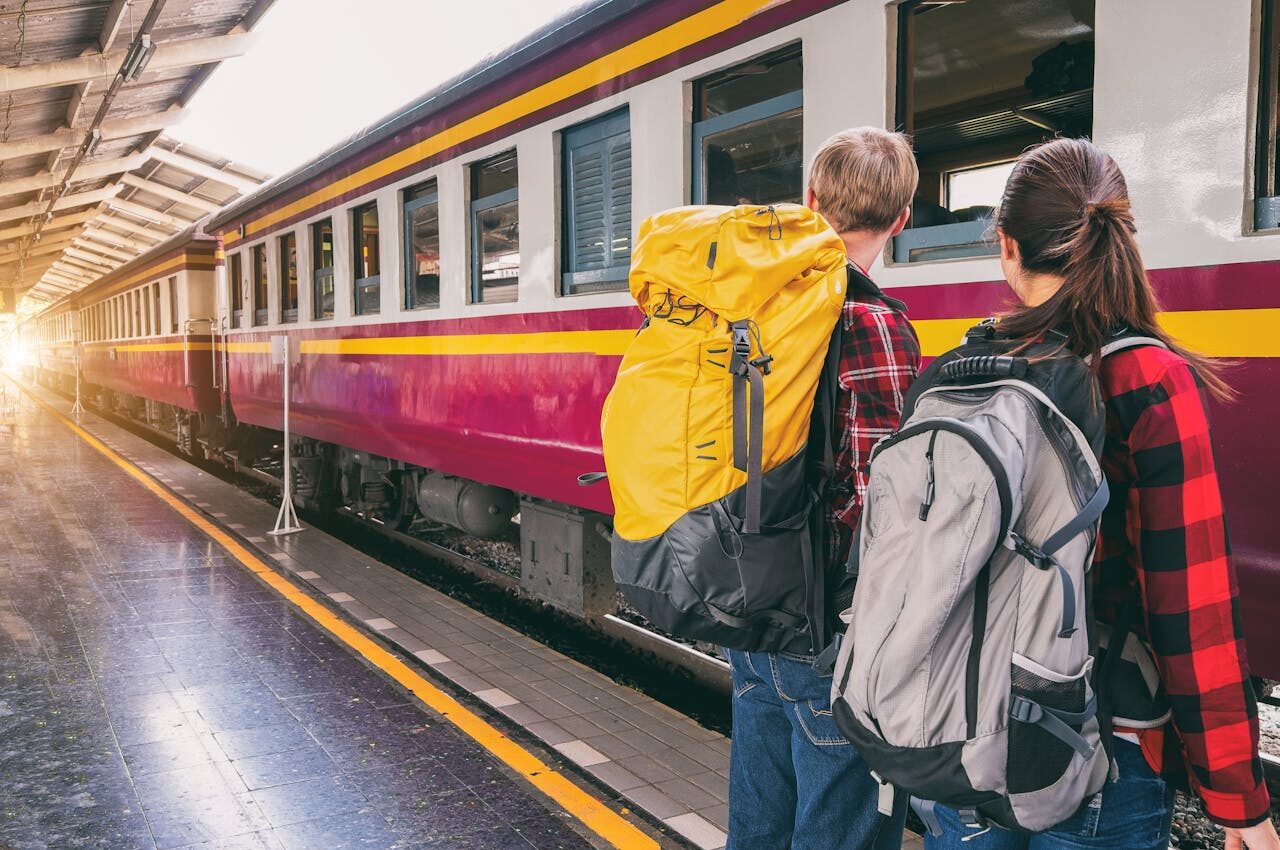 Mochileiros à espera na plataforma de uma estação de trem, prontos para uma aventura de viagem de trem.