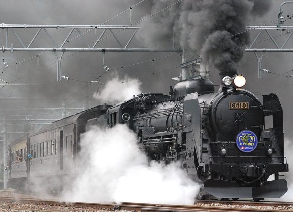 Locomotiva a vapor libertando fumo e vapor numa via férrea, mostrando o transporte ferroviário vintage.